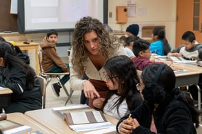 A middle school teacher helps two students during their test
