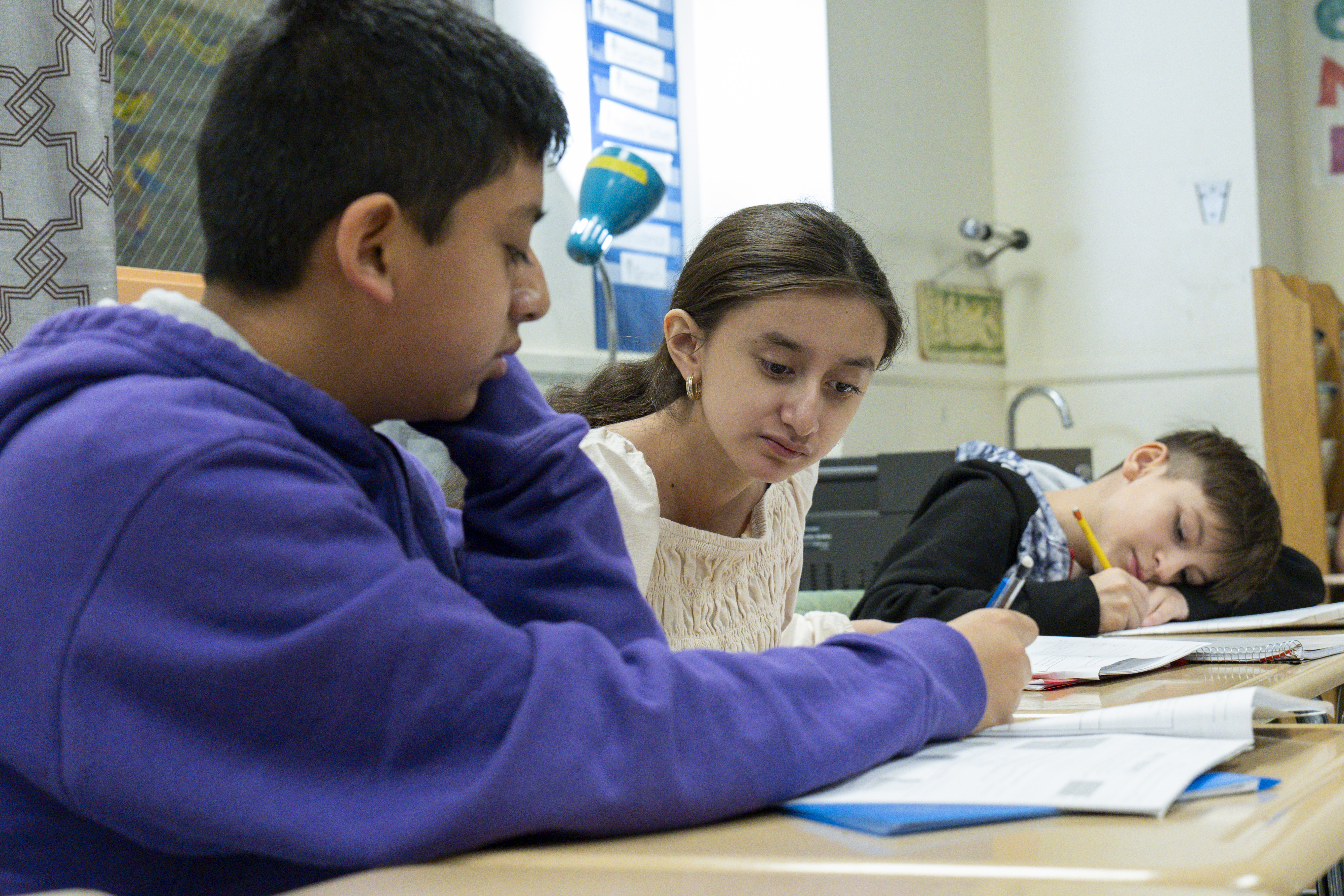 Photo of three middle school students at their desk collaborating on a workbook.
